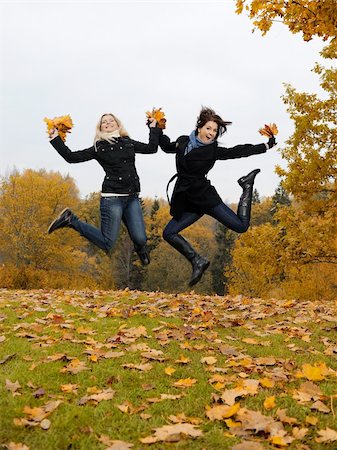 two beautiful girl friends with autumn leafs in a park jumping Stock Photo - Budget Royalty-Free & Subscription, Code: 400-05707155