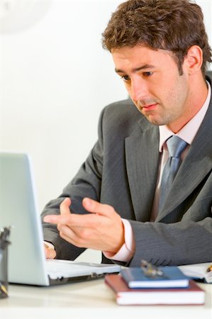 simsearch:400-04188055,k - Confused businessman sitting at office desk working on laptop Stock Photo - Budget Royalty-Free & Subscription, Code: 400-05708320