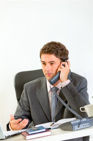 simsearch:400-06639907,k - Serious businessman sitting at office desk and speaking phone Stock Photo - Budget Royalty-Free & Subscription, Code: 400-05708321