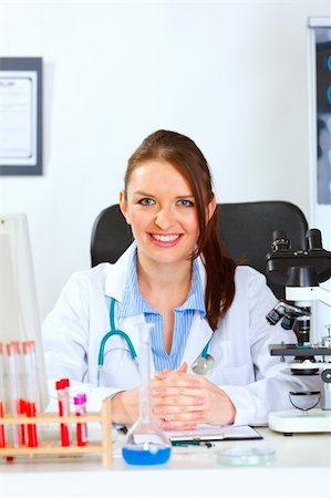 simsearch:400-04925813,k - Smiling female medical doctor sitting at table in cabinet Stock Photo - Budget Royalty-Free & Subscription, Code: 400-05701705