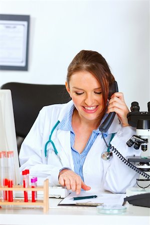 simsearch:400-07099889,k - Smiling female doctor talking on phone and looking in clipboard Stock Photo - Budget Royalty-Free & Subscription, Code: 400-05701715
