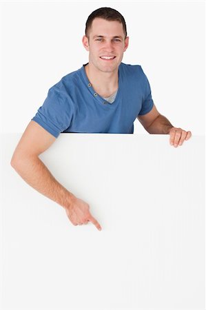 simsearch:400-05718227,k - Portrait of a smiling man pointing at a blank panel against a white background Stock Photo - Budget Royalty-Free & Subscription, Code: 400-05715313