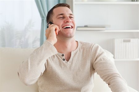 simsearch:400-05751258,k - Laughing man making a phone call while sitting on a couch in his living room Stock Photo - Budget Royalty-Free & Subscription, Code: 400-05715328