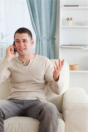 Portrait of a man talking through the phone while sitting on a couch in his living room Stock Photo - Budget Royalty-Free & Subscription, Code: 400-05715331
