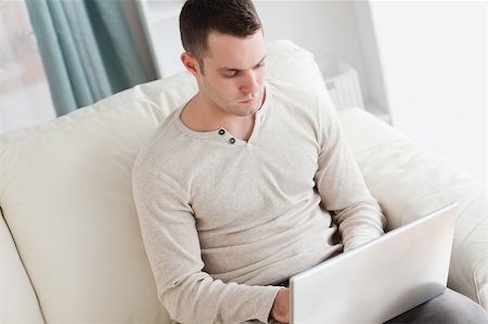 simsearch:400-05715585,k - Man using a laptop while sitting on a couch in his living room Foto de stock - Super Valor sin royalties y Suscripción, Código: 400-05715528