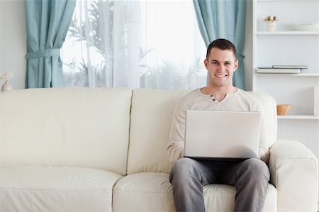 simsearch:400-05715661,k - Man using a laptop while sitting on a sofa in his living room Photographie de stock - Aubaine LD & Abonnement, Code: 400-05715523