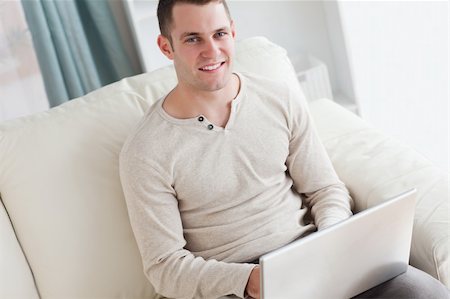 simsearch:400-05715661,k - Smiling man using a laptop while sitting on a couch in his living room Photographie de stock - Aubaine LD & Abonnement, Code: 400-05715530