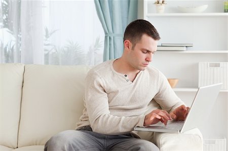 simsearch:400-05715528,k - Man typing on his laptop in his living room Stock Photo - Budget Royalty-Free & Subscription, Code: 400-05715541