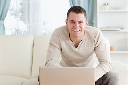 simsearch:400-05715661,k - Smiling young man using a notebook in his living room Photographie de stock - Aubaine LD & Abonnement, Code: 400-05715565