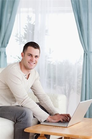 simsearch:400-05715585,k - Portrait of a smiling man typing on his laptop in his living room Foto de stock - Super Valor sin royalties y Suscripción, Código: 400-05715606