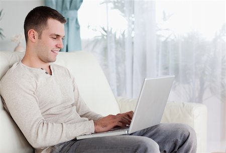 simsearch:400-05715528,k - Happy man typing on his laptop in his living room Stock Photo - Budget Royalty-Free & Subscription, Code: 400-05715607