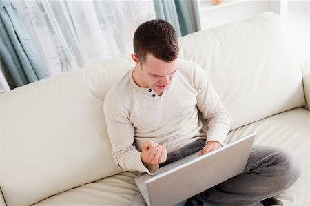 simsearch:400-05742016,k - Victorious man using a notebook in his living room Stock Photo - Budget Royalty-Free & Subscription, Code: 400-05715602