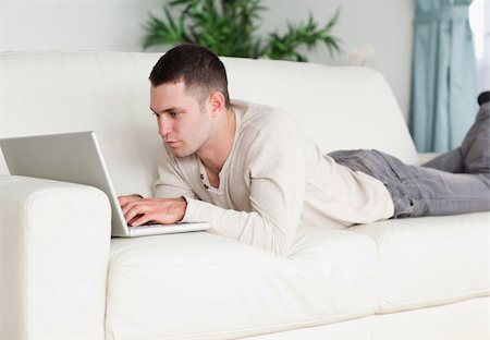 simsearch:400-05715585,k - Young man lying on a sofa using a laptop in his living room Foto de stock - Super Valor sin royalties y Suscripción, Código: 400-05715658