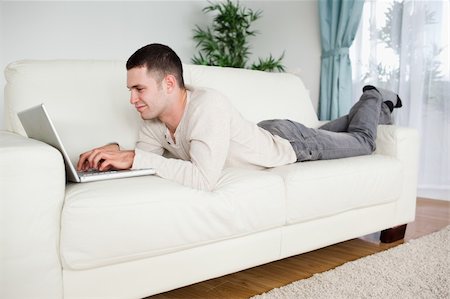 simsearch:400-05715661,k - Handsome man lying on a couch using a notebook in his living room Photographie de stock - Aubaine LD & Abonnement, Code: 400-05715665