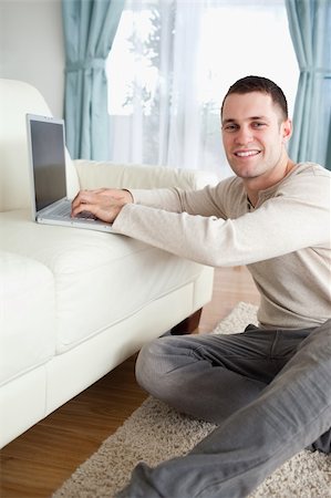 simsearch:400-05715528,k - Portrait of a smiling man sitting on a carpet with a laptop while looking at the camera Stock Photo - Budget Royalty-Free & Subscription, Code: 400-05715675