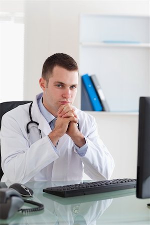 simsearch:400-05710928,k - Thinking young doctor sitting behind desk Stockbilder - Microstock & Abonnement, Bildnummer: 400-05710456