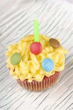 fancy candle - Fancy birthday cupcake decorated with small colorful sugar-coated chocolate confectionery on a transparent glass dish, over a white background. Selective focus. Stock Photo - Budget Royalty-Free & Subscription, Code: 400-05711085