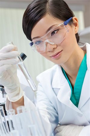 A Chinese Asian female medical or scientific researcher or doctor using looking at a test tube of clear liquid in a laboratory with her colleague out of focus behind her. Stock Photo - Budget Royalty-Free & Subscription, Code: 400-05711197