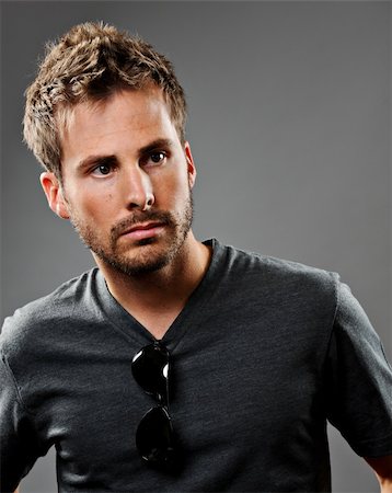 Young beautiful male model wearing a gray t-shirt. He has a serious expression and is shot on a gray background. Photographie de stock - Aubaine LD & Abonnement, Code: 400-05728325