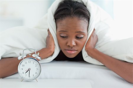 simsearch:400-04903814,k - Tired woman covering her ears with a duvet while looking at her alarm clock Foto de stock - Royalty-Free Super Valor e Assinatura, Número: 400-05729401