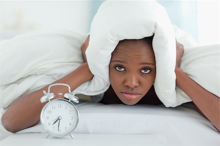 simsearch:6109-06194408,k - Exhausted woman covering her ears with a duvet while her alarm clock is ringing Stockbilder - Microstock & Abonnement, Bildnummer: 400-05729402