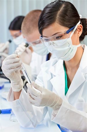 A Chinese Asian female medical or scientific researcher or doctor using looking at a test tube of clear liquid in a laboratory with her colleagues out of focus behind her. Stock Photo - Budget Royalty-Free & Subscription, Code: 400-05721386
