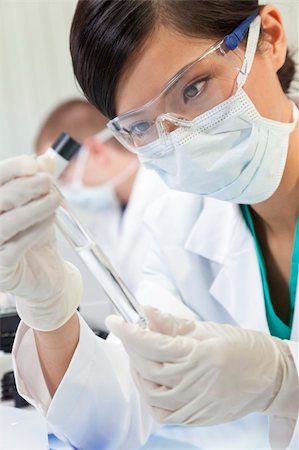 A Chinese Asian female medical or scientific researcher or doctor using looking at a test tube of clear liquid in a laboratory with her colleague out of focus behind her. Stock Photo - Budget Royalty-Free & Subscription, Code: 400-05721389