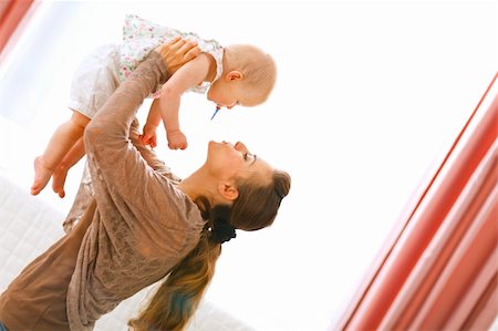 simsearch:400-05899075,k - Young mama playing with baby by rising her up at home Fotografie stock - Microstock e Abbonamento, Codice: 400-05723081