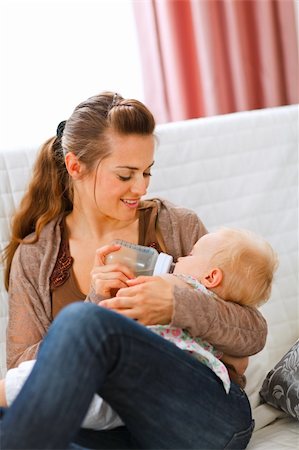 simsearch:400-05899075,k - Young mother sitting on sofa and feeding her baby  at home Fotografie stock - Microstock e Abbonamento, Codice: 400-05723091