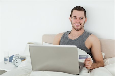 einkaufssüchtiger (männlich) - Young man shopping online in his bedroom Stockbilder - Microstock & Abonnement, Bildnummer: 400-05737455