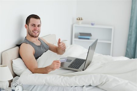 shopaholic bedroom - Happy man purchasing online with thumb up in his bedroom Stock Photo - Budget Royalty-Free & Subscription, Code: 400-05737464