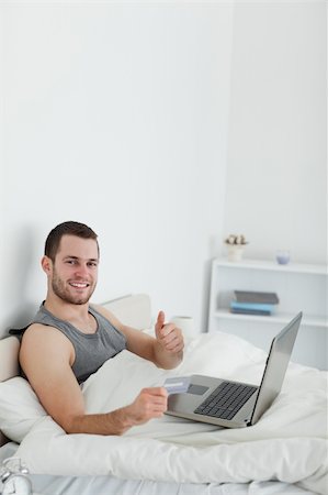 einkaufssüchtiger (männlich) - Portrait of a man purchasing online with thumb up in his bedroom Stockbilder - Microstock & Abonnement, Bildnummer: 400-05737465