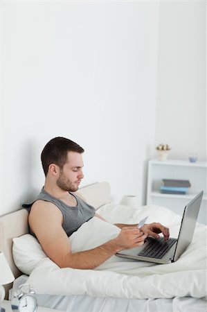 shopaholic bedroom - Portrait of a man booking his holidays online in his bedroom Stock Photo - Budget Royalty-Free & Subscription, Code: 400-05737466