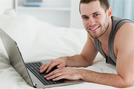 Handsome man using a laptop while lying on his belly in his bedroom Stock Photo - Budget Royalty-Free & Subscription, Code: 400-05737469