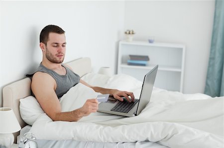 einkaufssüchtiger (männlich) - Young man purchasing online in his bedroom Stockbilder - Microstock & Abonnement, Bildnummer: 400-05737461