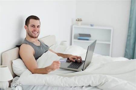 shopaholic bedroom - Smiling man purchasing online in his bedroom Stock Photo - Budget Royalty-Free & Subscription, Code: 400-05737463