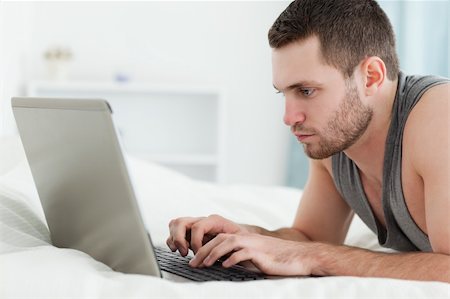Focused man using a laptop while lying on his belly in his bedroom Stock Photo - Budget Royalty-Free & Subscription, Code: 400-05737472