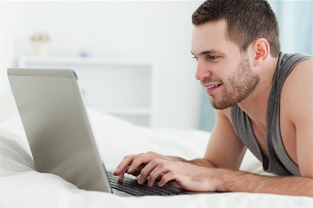 Smiling man using a laptop while lying on his belly in his bedroom Stock Photo - Budget Royalty-Free & Subscription, Code: 400-05737473