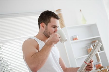 simsearch:400-05737647,k - Young man drinking tea while reading the news in his kitchen Stock Photo - Budget Royalty-Free & Subscription, Code: 400-05737576