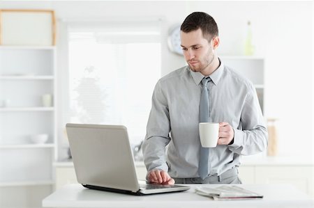 simsearch:400-05737647,k - Businessman using a laptop while drinking coffee in his kitchen Stock Photo - Budget Royalty-Free & Subscription, Code: 400-05737649
