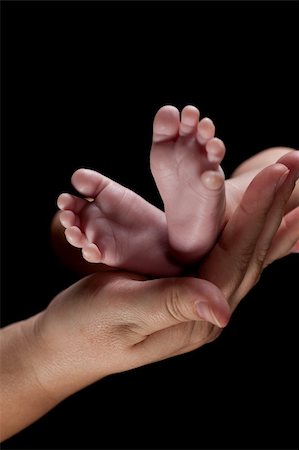 A newborn's tiny feet held gently in mom's hand. Studio shot on a black background. Stock Photo - Budget Royalty-Free & Subscription, Code: 400-05738411