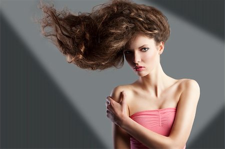 simsearch:400-06102733,k - beauty fashion portrait of beautiful young brunette with curly hair flying and creative hairstyle. she looks in to the lens, her hair are raised on the right anche she takes right shoulder with left hand. Fotografie stock - Microstock e Abbonamento, Codice: 400-05744994
