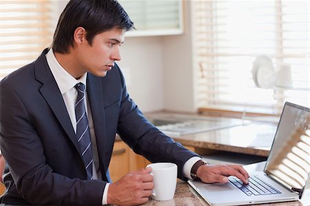 simsearch:400-05737647,k - Man working with a laptop while drinking coffee in his kitchen Stock Photo - Budget Royalty-Free & Subscription, Code: 400-05746909