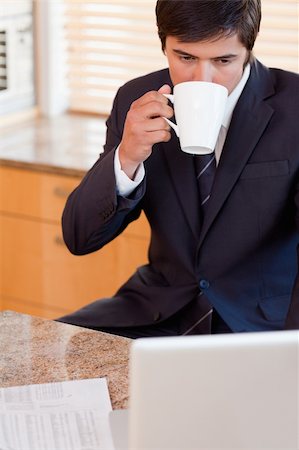 simsearch:400-05737647,k - Portrait of a businessman drinking coffee while using a laptop in his kitchen Stock Photo - Budget Royalty-Free & Subscription, Code: 400-05746902