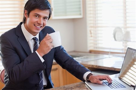 Man working with a notebook while drinking coffee in his kitchen Stock Photo - Budget Royalty-Free & Subscription, Code: 400-05746912