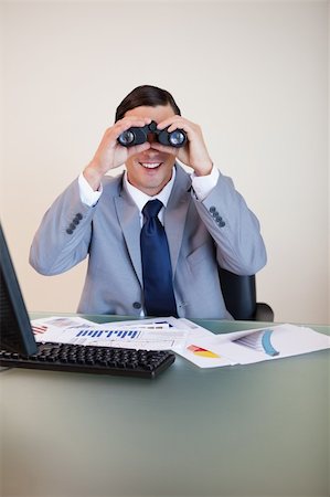 simsearch:400-05748158,k - Smiling businessman at his desk looking through binoculars Stock Photo - Budget Royalty-Free & Subscription, Code: 400-05748170