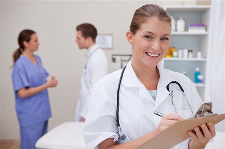 Smiling doctor writing on clipboard with colleagues behind her Stock Photo - Budget Royalty-Free & Subscription, Code: 400-05748242