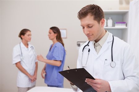 Doctor reading patients record with colleagues behind him Stock Photo - Budget Royalty-Free & Subscription, Code: 400-05748243