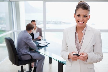 Smiling marketing manager holding cellphone with her team sitting behind her Stock Photo - Budget Royalty-Free & Subscription, Code: 400-05748342