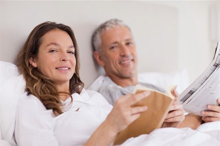 simsearch:400-05749447,k - Smiling woman reading a book while her husband is reading the news in their bedroom Stock Photo - Budget Royalty-Free & Subscription, Code: 400-05749452